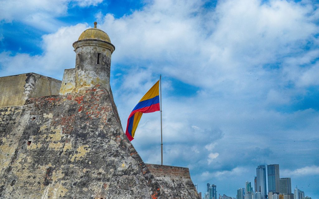 Torre do Castillo de San Felipe de Barajas ao lado da bandeira, contrastando com edifícios modernos ao fundo.