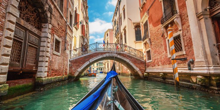 Barco em canal de Veneza, na Itália, em meio a construções antigas