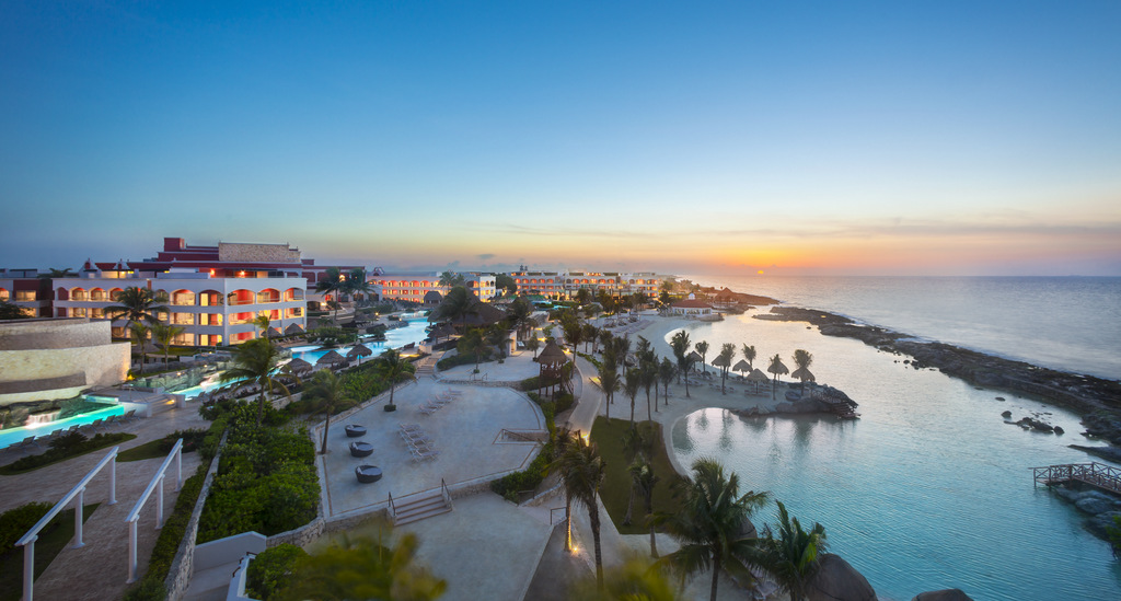 Pôr do sol ao fundo, com o mar à direita e a piscina natural do Hard Rock Hotel Riviera Maya